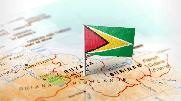 Imagem de um mapa com enfoque no território da Guiana, e a bandeira do país fincada no mapa. Foto: MarkRubens/Getty Images.