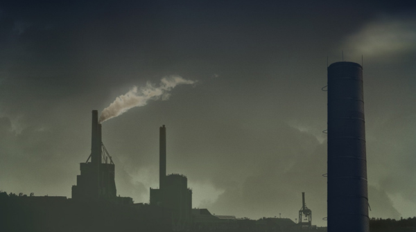 Imagem com um filtro acinzentado de uma fábrica com torres soltando fumaça. Foto: PxHere.