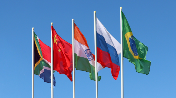 Imagem das bandeiras da África do Sul, da China, da Índia, da Rússia e do Brasil hasteadas lado a lado; no fundo, o céu azul. Foto: Oleg Elkov Getty Images via Canva.